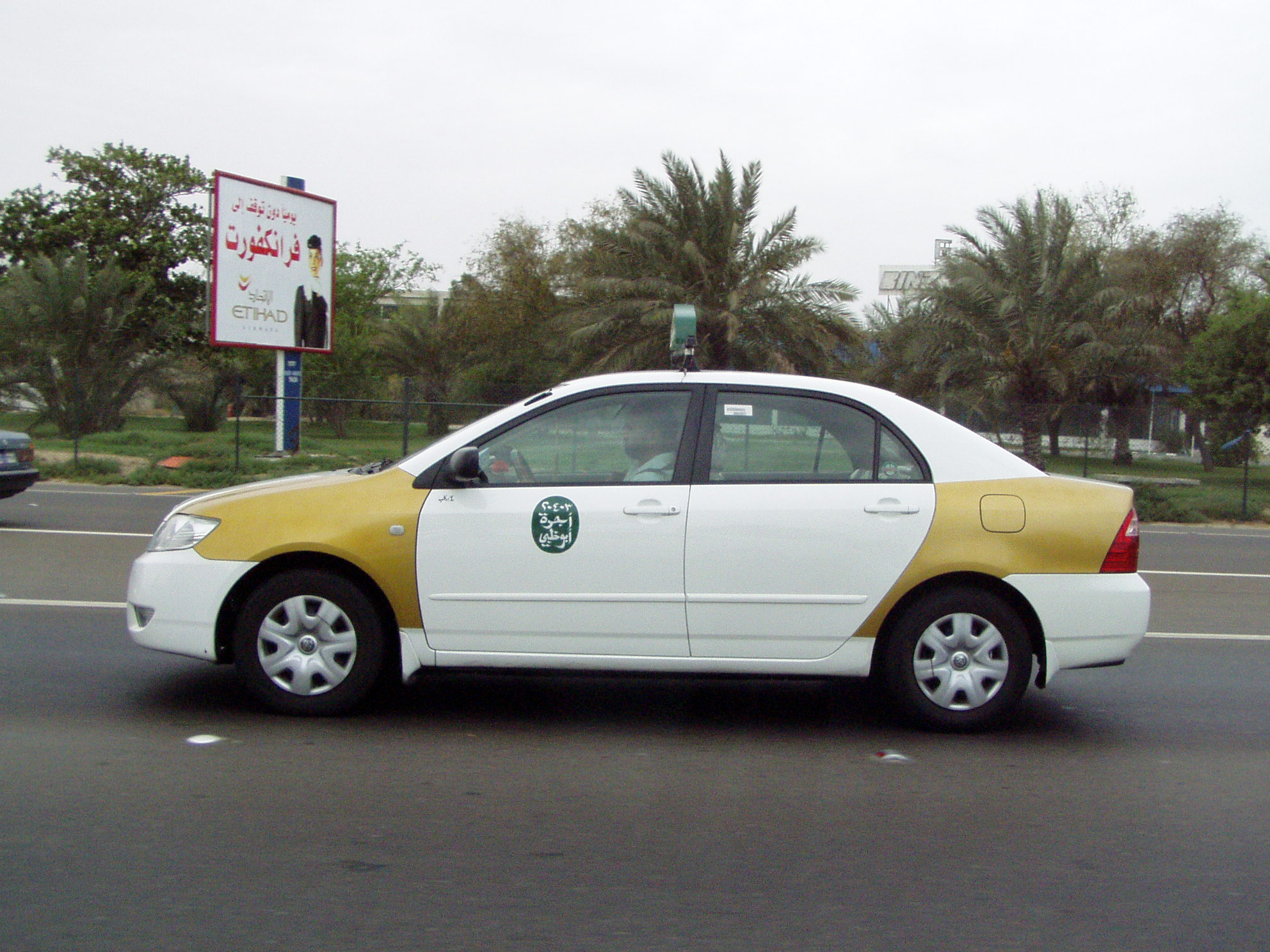 Side view of a white-and-gold Abu Dhabi taxi on a road. Historical June 2005 photograph, not the new airport fleet.